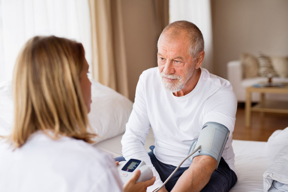 Pflegerin während einer Blutdruckmessung eines älteren Mannes.