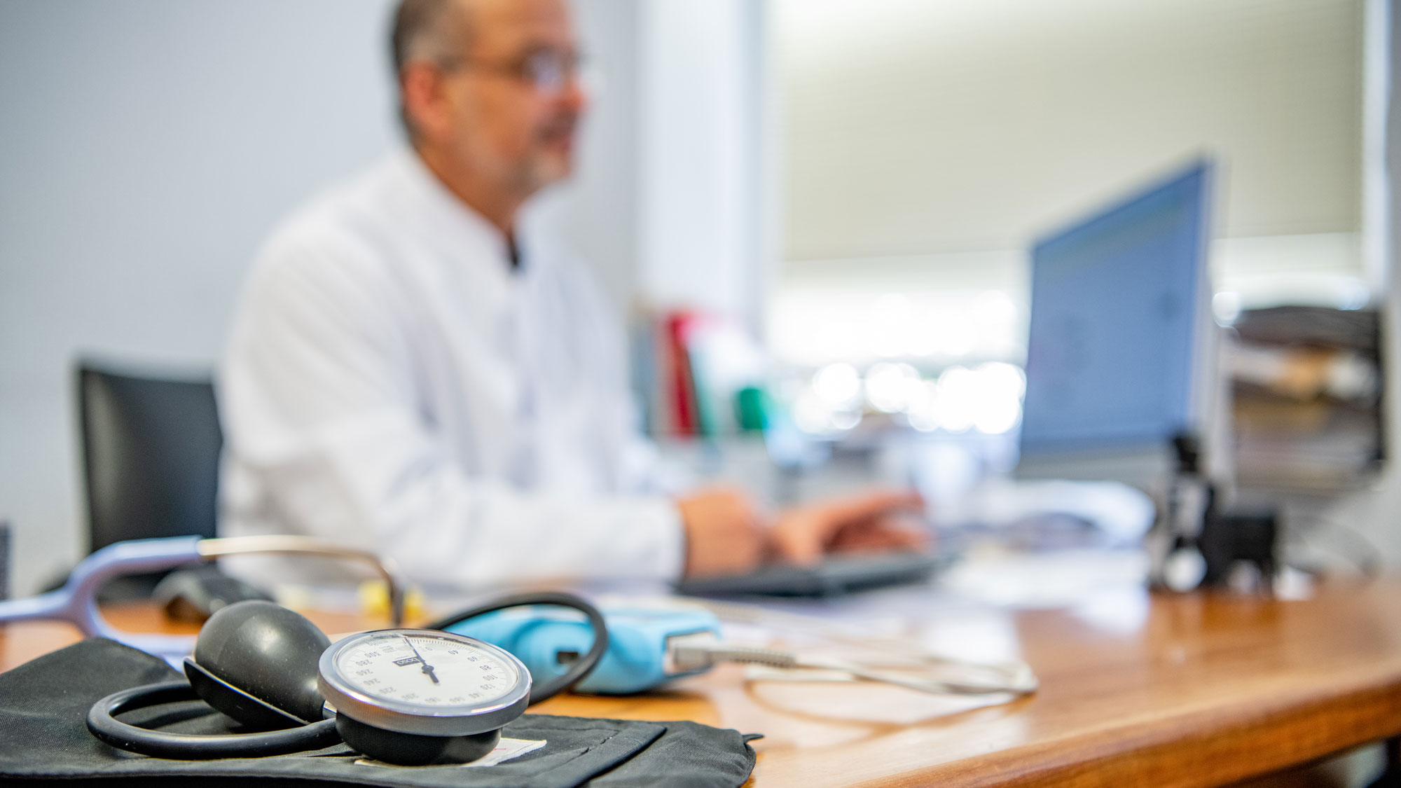 Ein Arzt an seinem Tisch mit einem Blutdruckmessgerät